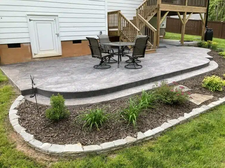 Rounded concrete patio with table and chairs beside deck steps
