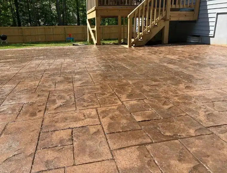 Earth-toned stamped concrete patio beside wooden deck stairs